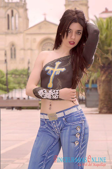 black haired woman in front of a church in full body paint that includes a black top featuring a cross with interesting detail and very detailed jeans